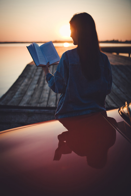 Woman sitting on car and reading book